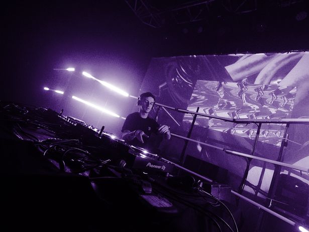 DJ on Pioneer decks in front of a projection screen showing abstract visuals